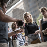 An image of a young woman bartender pouring a small glass of beer for two other young women patrons at the Beer Fest