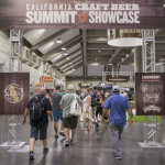 an image of some Craft Beer Summit goers walking through Cal Expo with a sign above them that reads 'California Craft Beer Summit Showcase'
